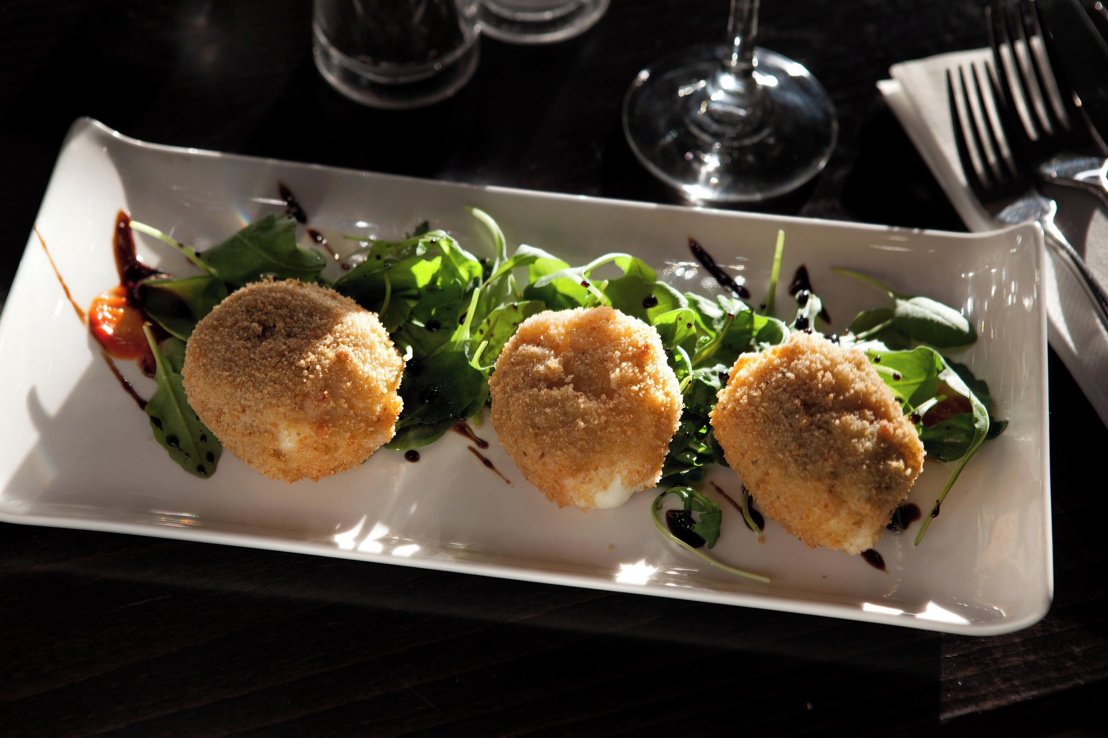 A rectangular white plate with three round, breaded items and a green salad.