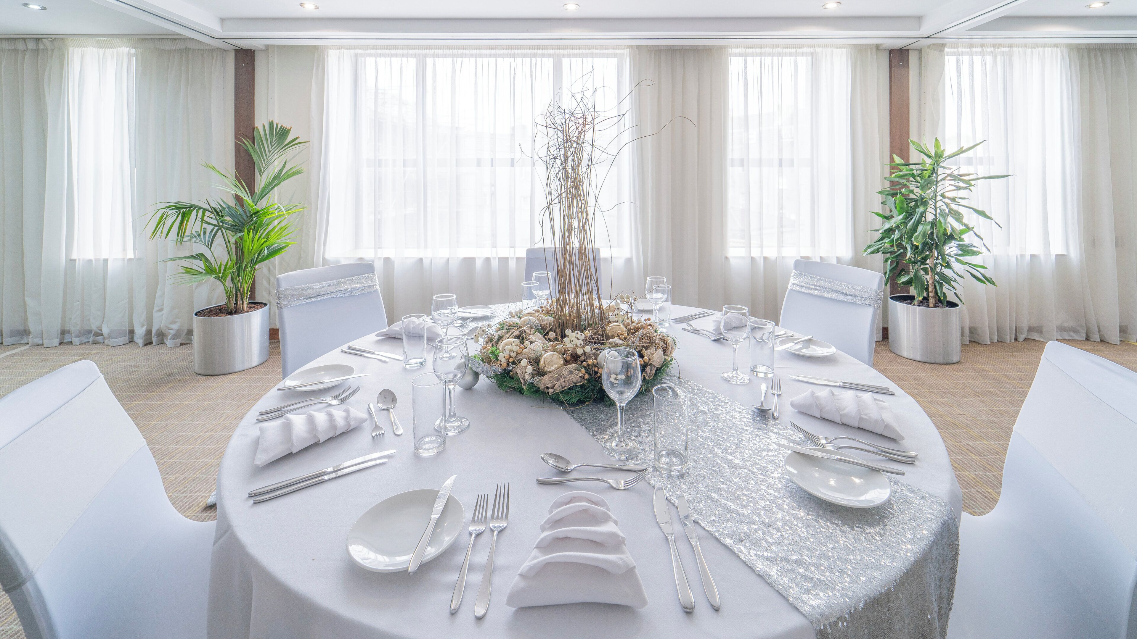 A round table set for a formal event with white tablecloth, silverware, and a centerpiece.