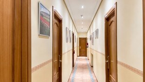 A hotel hallway with wooden doors, a patterned carpet, and framed pictures on the walls. - Luz Madrid Rooms (Madrid)