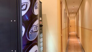 A hotel hallway with a vending machine on the left, a door at the end, and a tiled floor. - Luz Madrid Rooms (Madrid)