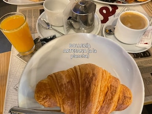 Un ambient de petit esmorzar amb un croissant a un plat, un got de suc d'aranja, una tassa de cafè i una teiera sobre una taula.