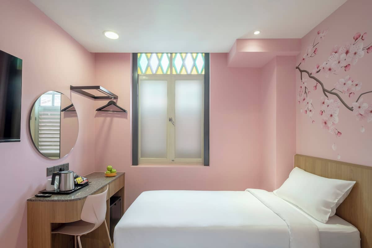 Quarto de hotel com duas camas, uma escrivaninha com chaleira, um espelho e uma janela com persianas.