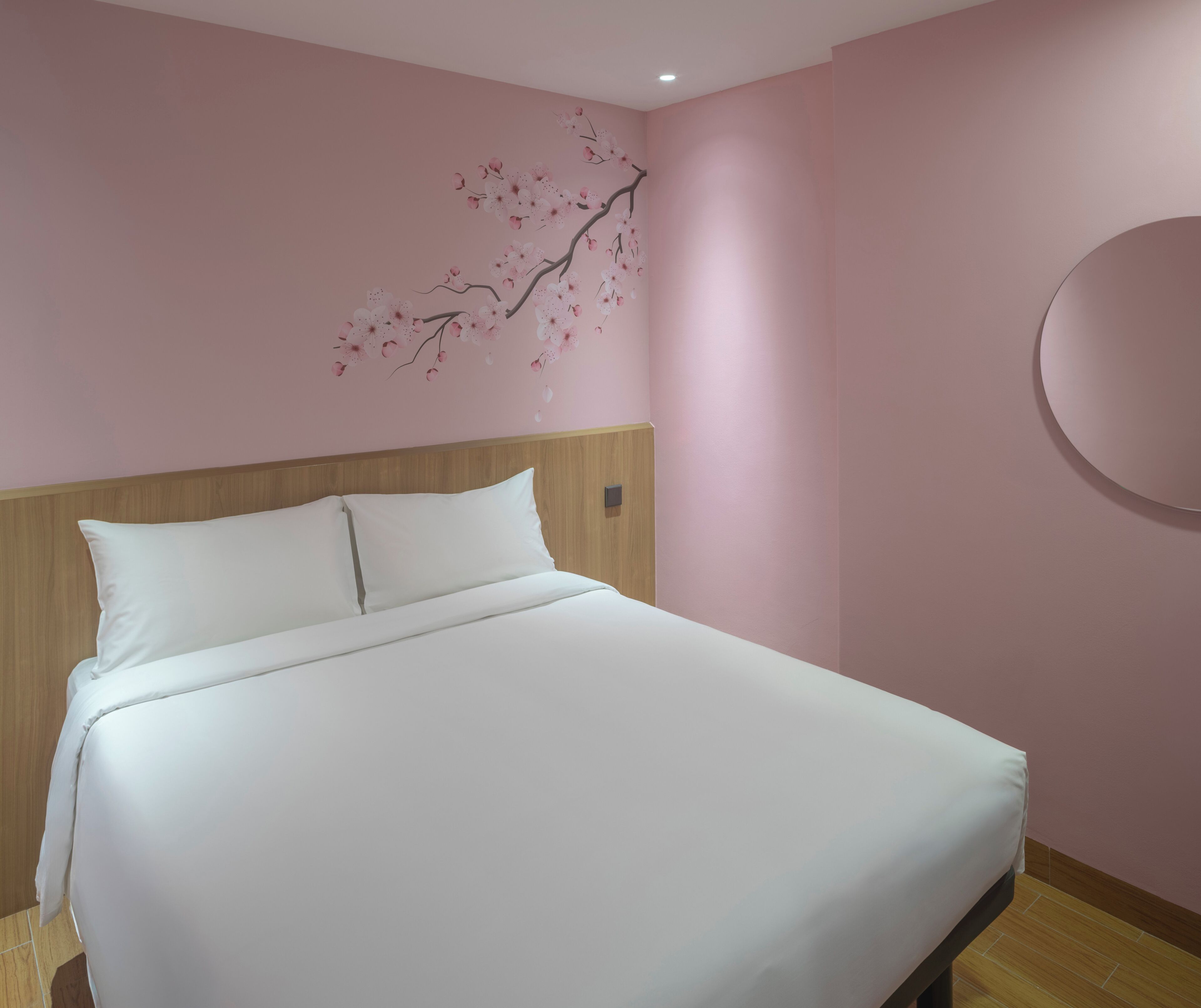 A neatly made bed with white linens in a room with pink walls and a wooden headboard.
