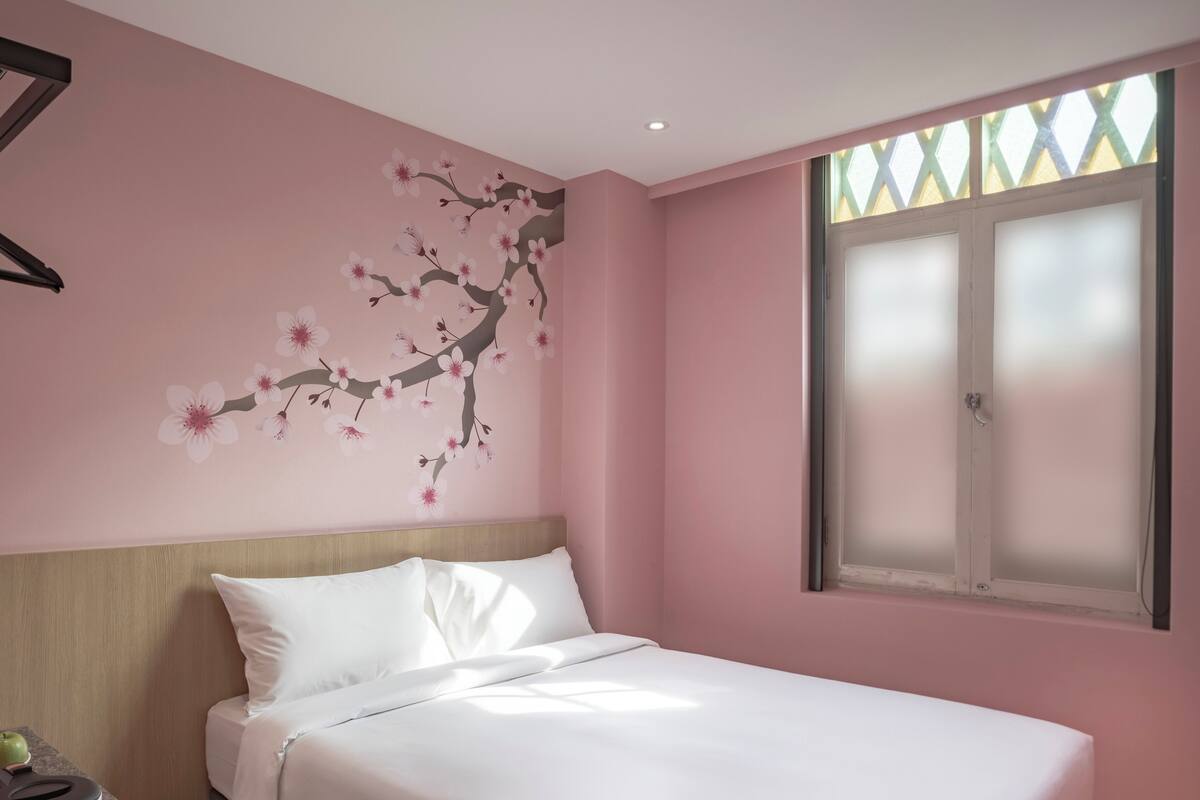 Uma cama bem arrumada em quarto com paredes cor-de-rosa, janela com vidro fosco e ar condicionado fixado na parede.
