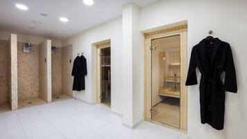 A spacious bathroom with white tiled floors, a wooden sauna, and black robes hanging on the wall.