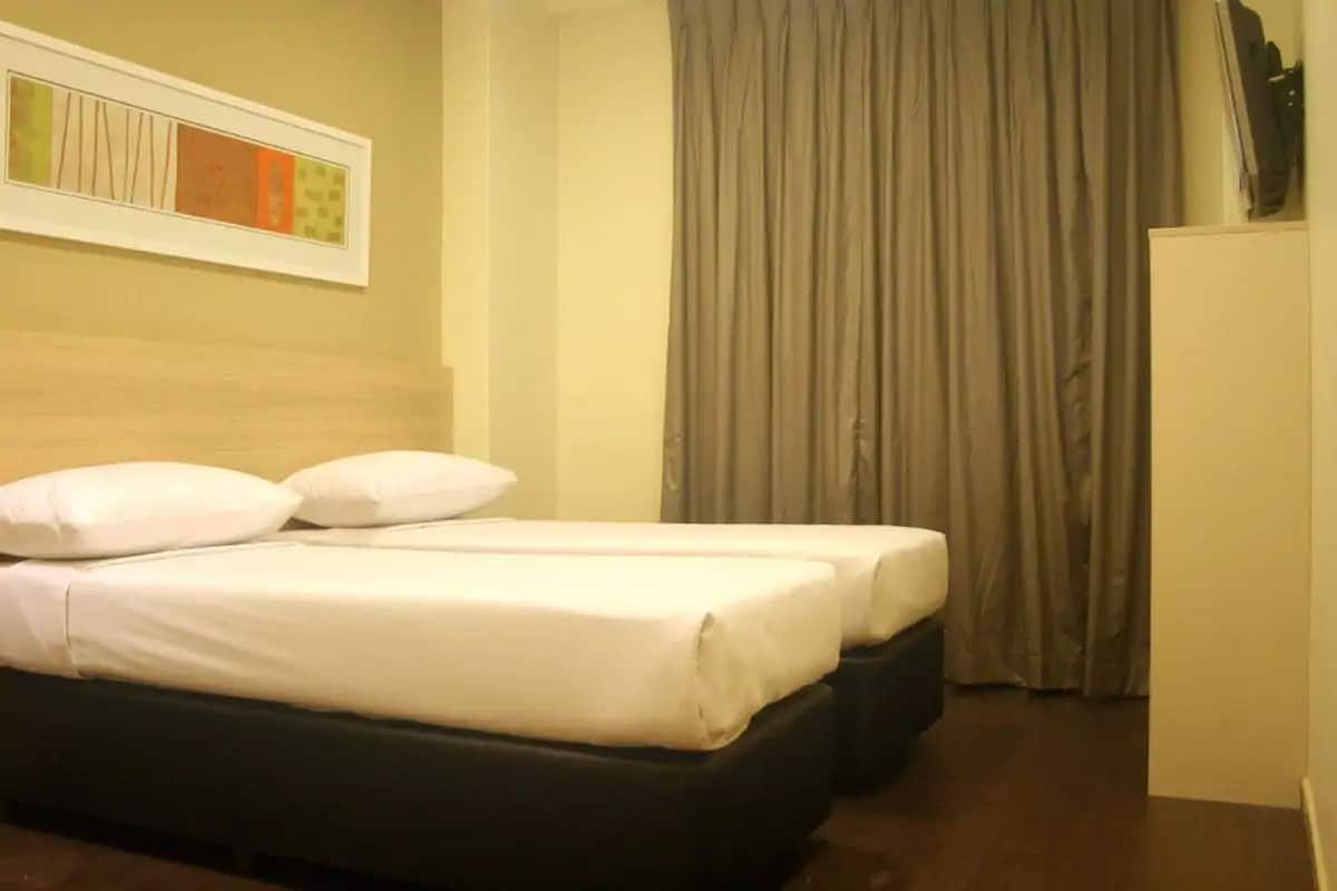 Quarto de hotel com cama, televisão e janela com cortinas.