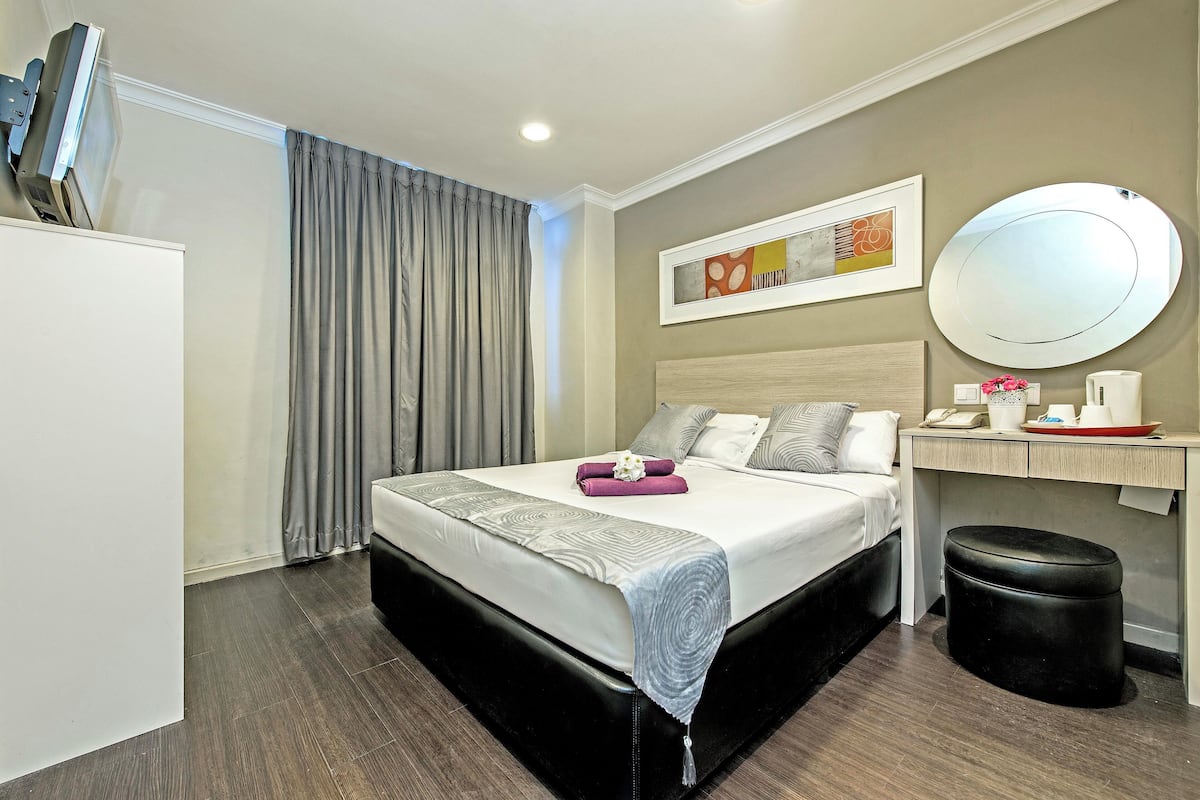 Quarto de hotel com cama, mesa de cabeceira, espelho e um banquinho.
