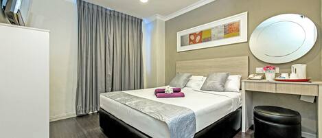 Una habitación de hotel con cama, mesita de noche, espejo y un taburete pequeño.