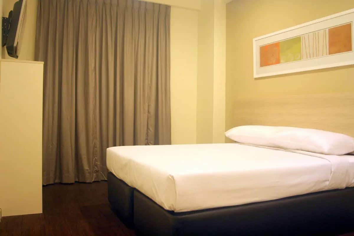 Quarto de hotel com cama, cortinas, uma obra de arte emoldurada na parede e uma TV de tela plana na parede.