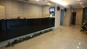 A hotel reception area with a black reception desk, a television screen, and Christmas decorations. - Hotel 81 Lucky (Singapore)