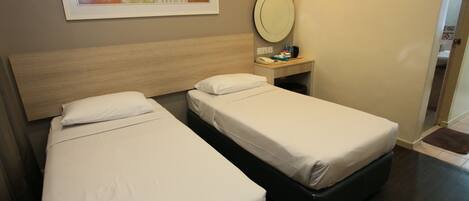 A hotel room with two single beds, a bedside table with a mirror, and a framed artwork on the wall.