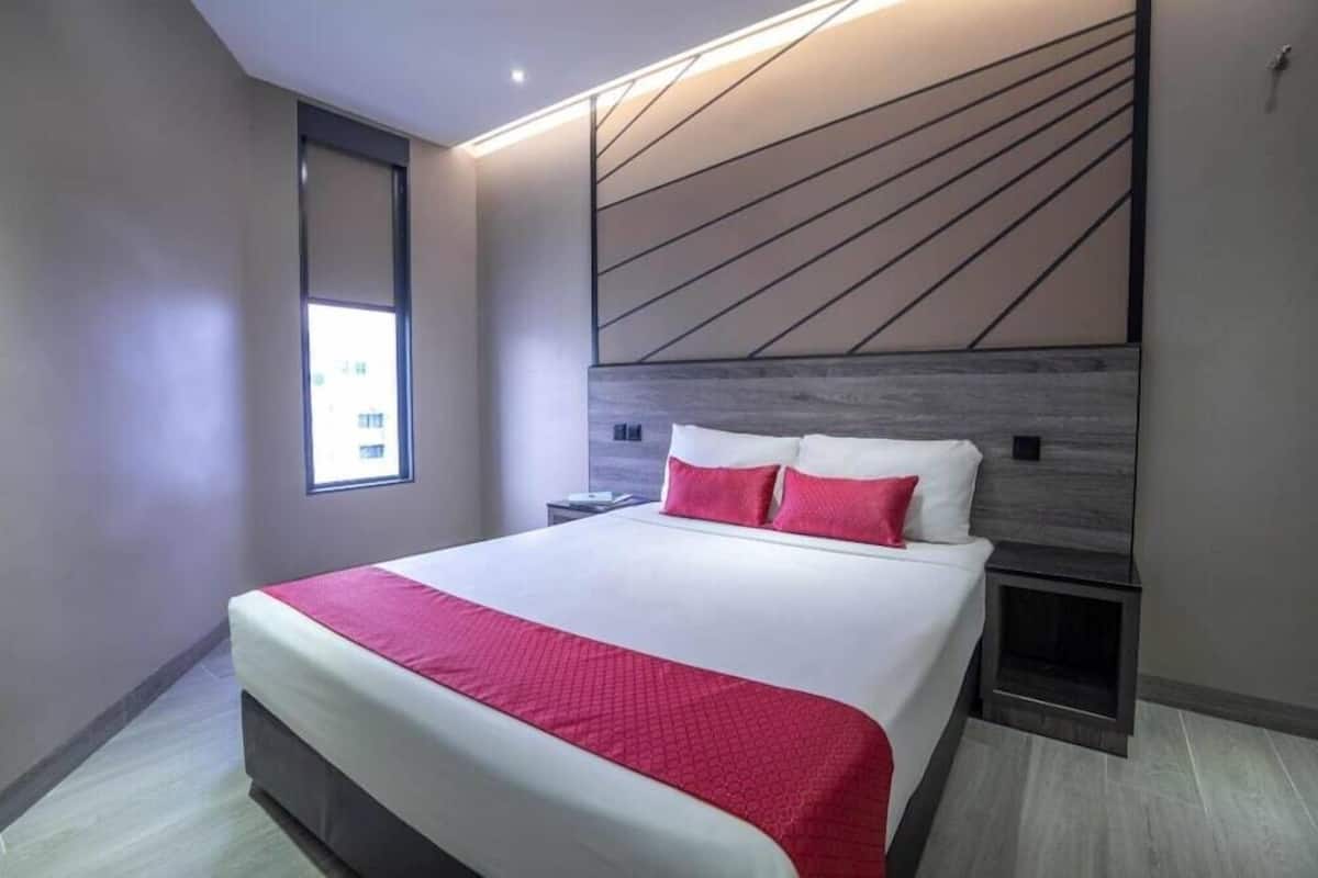 Quarto de hotel moderno com uma cama grande, uma mesinha de cabeceira, televisão integrada e uma janela.
