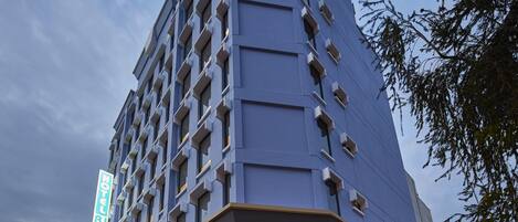 Un hotel moderno con un llamativo letrero de 'HOTEL 81', que cuenta con una entrada en esquina, ventanas grandes y fachada de vidrio.