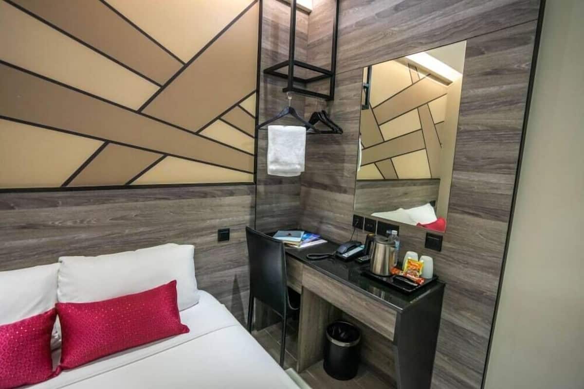 Quarto de hotel com cama, escrivaninha com computador, espelho e porta-toalhas.