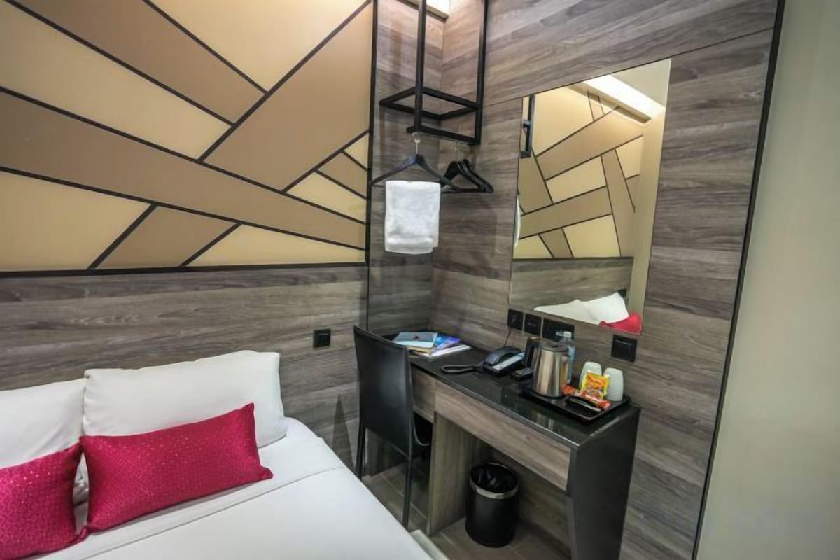 Une chambre d’hôtel avec un lit, un bureau, un miroir et une poubelle.