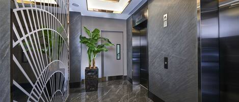 A modern elevator interior with metallic walls and a marble floor.