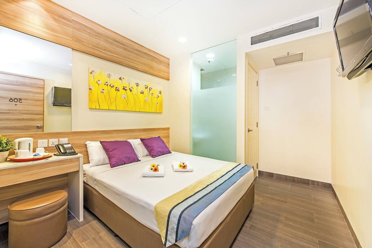 A hotel room with a bed, bedside table, and a desk with a chair.