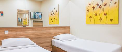 Habitación de hotel con dos camas individuales, un cabecero de madera, un espejo grande y dos cuadros en la pared.