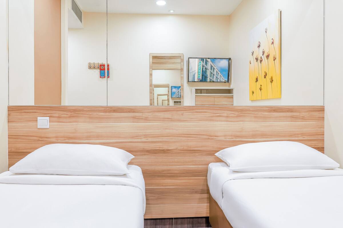 A hotel room with two beds, a wooden headboard, a flat-screen TV, a painting, and a mirror.
