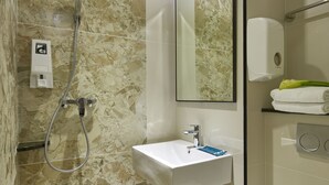 Un baño con ducha de mármol, lavabo con dispensador de jabón y espejo.