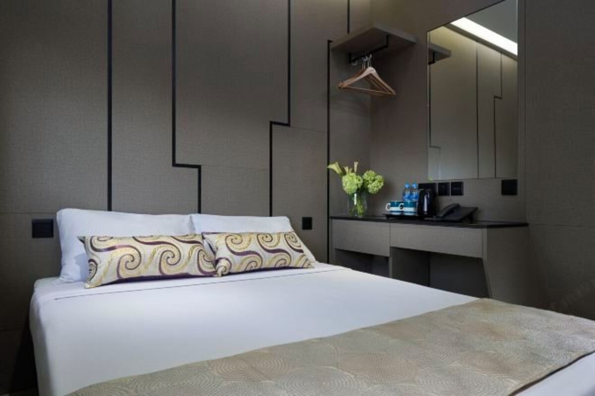 A modern hotel room with a large bed, a bedside table with a mirror, and a small desk area.