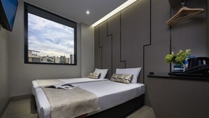 Una habitación de hotel moderna con dos camas, un ventanal con vistas a la ciudad, un escritorio con una planta y una lámpara colgante.