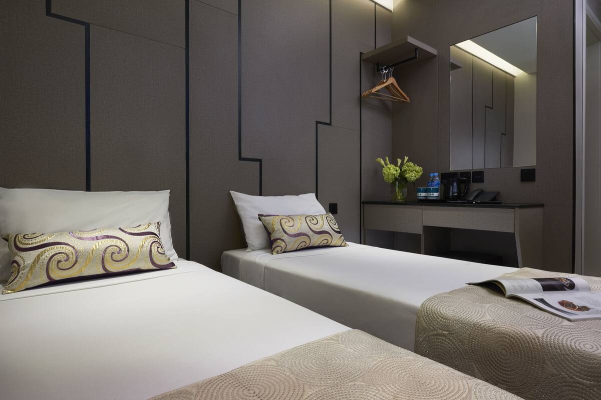 Quarto de hotel com duas camas, um espelho, uma secretária pequena e um cabideiro.