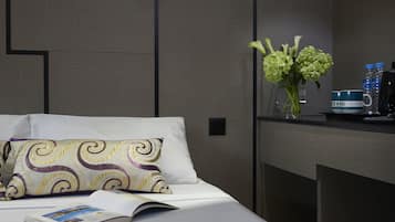 Una cama bien hecha con un cojín estampado, un libro y un florero con flores sobre una mesita de noche.