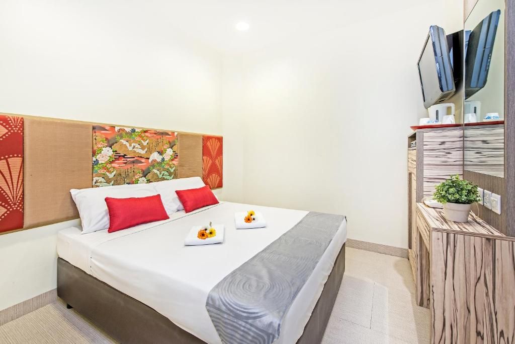 A hotel room with a bed, a bedside table with a plant, and a wall-mounted TV.