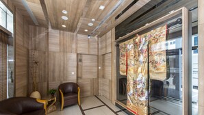 A modern lobby with a wooden floor, a leather sofa, a glass partition, and a traditional curtain. - Hotel 81 Osaka (Singapore)