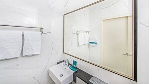 A bathroom with a marble wall, a sink, a mirror, and a towel rack. - Hotel 81 Osaka (Singapore)