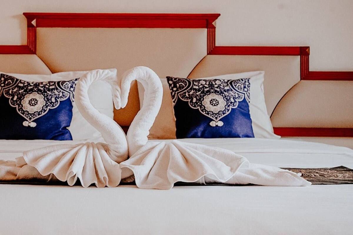 A bed with a heart-shaped towel arrangement and two patterned pillows.