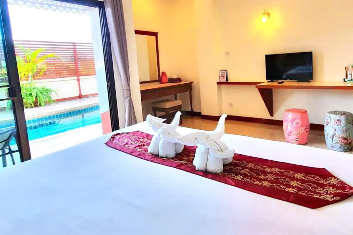 A hotel room with a bed, a TV, a desk, a refrigerator, a window with a view of a pool, and a balcony.