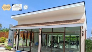 A modern hotel with large glass windows, a covered patio, and a sign indicating COVID-19 safety measures. - Mei Zhou Phuket Hotel (Phuket)