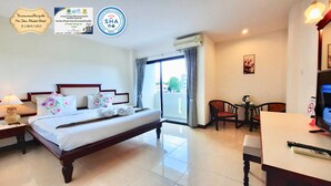 A hotel room with a bed, a desk, a chair, and a TV. There is a window with curtains and an air conditioning unit above the window. - Mei Zhou Phuket Hotel (Phuket)