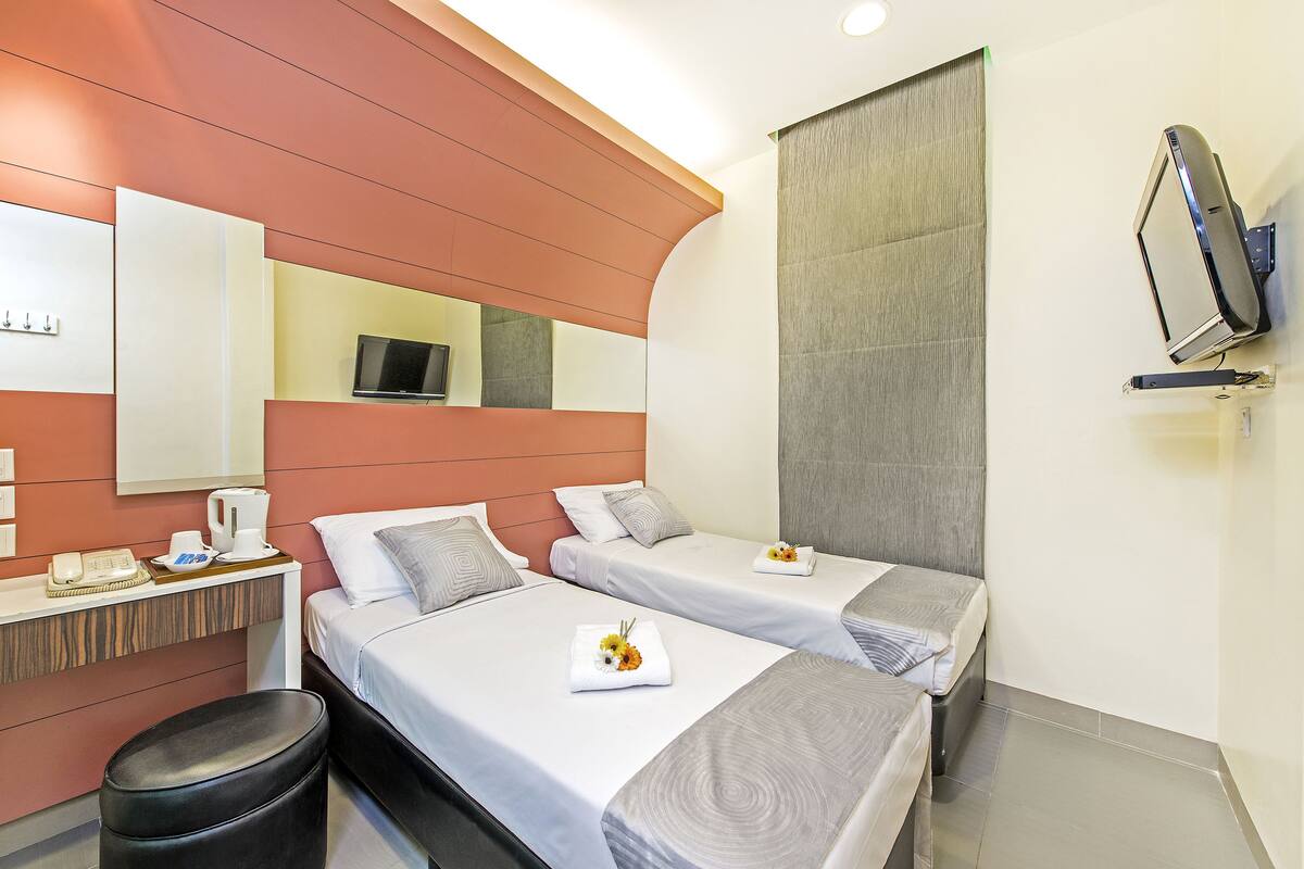 A hotel room with two beds, a desk with a telephone and a coffee maker, a mirror, and a TV mounted on the wall.