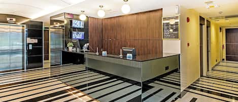 Un espace d’accueil d’hôtel comprenant un écran numérique, un comptoir d’accueil et un guichet d’enregistrement.