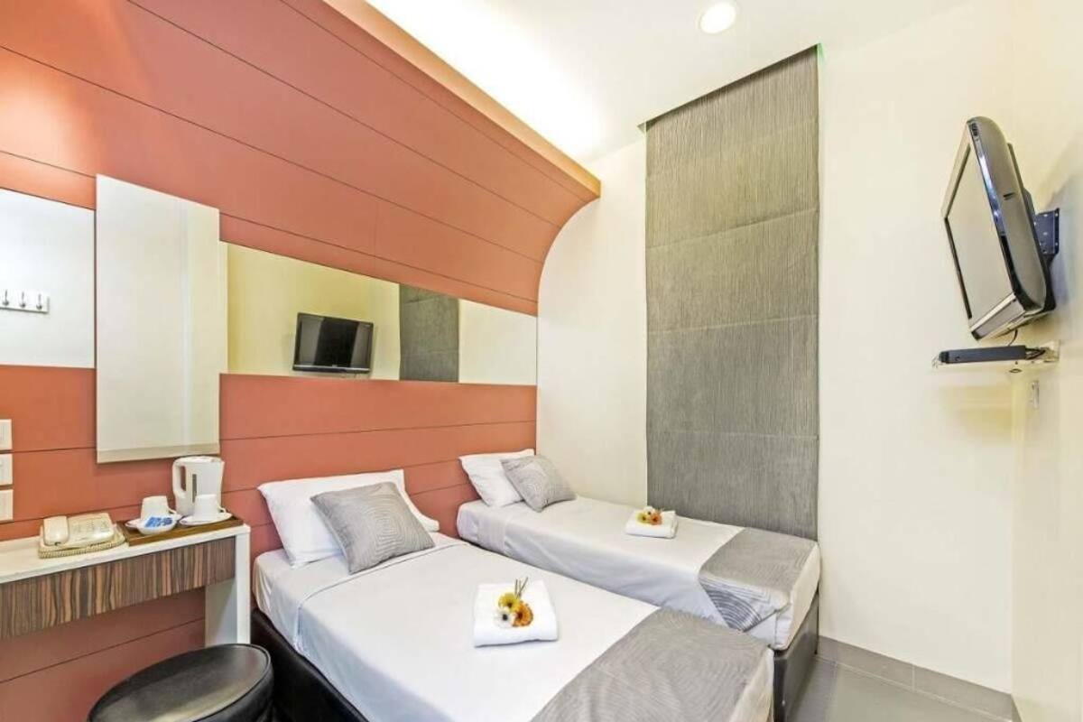 A hotel room with two beds, a flat-screen TV mounted on the wall, a small table with a phone and a coffee maker, and a trash bin.
