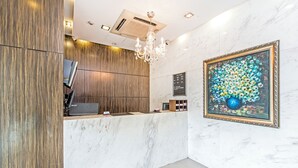 A reception area with a marble counter, wooden paneling, a chandelier, and a framed floral artwork. - Hotel 81 Bugis (Singapore)