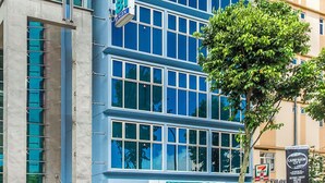 A modern hotel with a prominent sign, large windows, and a tree in front. - Hotel 81 Bugis (Singapore)