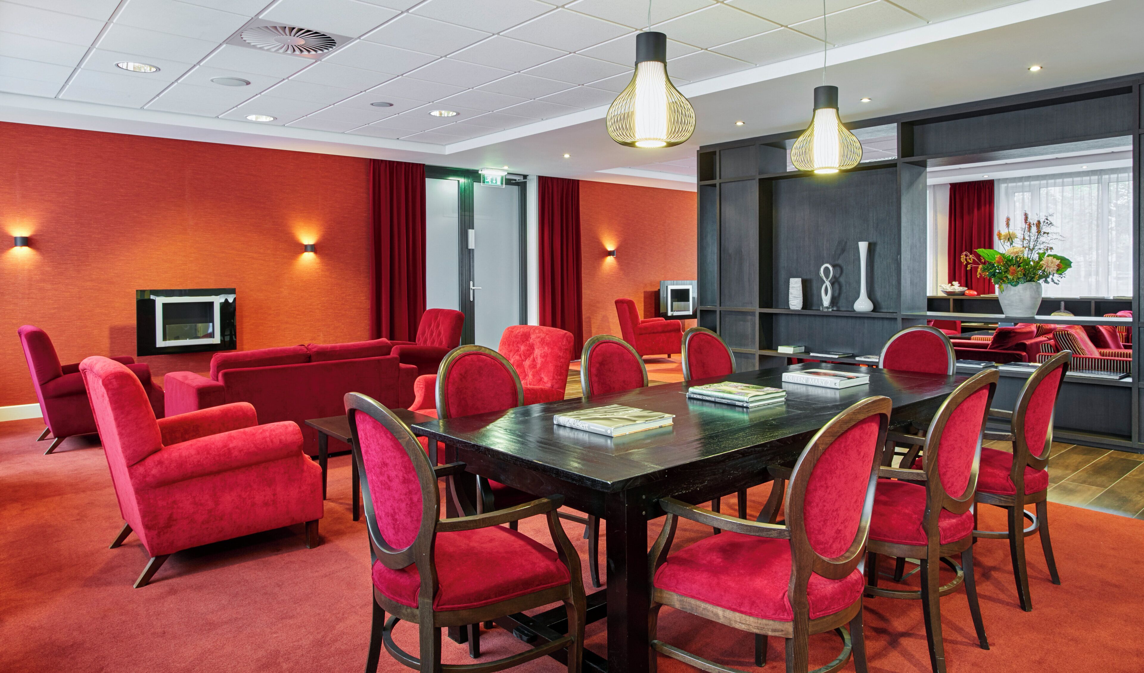 Un salón de conferencias con una larga mesa y sillas rojas, una televisión y una estantería con objetos decorativos.