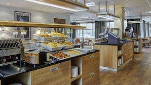 A buffet area with various food options, a self-service beverage station, and a seating area with tables and chairs. - Holiday Inn Express Amsterdam - Schiphol by IHG (Hoofddorp)
