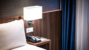 Une chambre d’hôtel avec une tête de lit en bois, une lampe de chevet, un téléphone et un oreiller blanc.