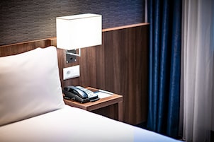 A hotel room with a wooden headboard, a bedside lamp, a telephone, and a white pillow.