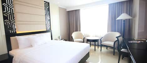 A hotel room with a large bed, two armchairs, a small table, and a desk with a lamp.