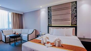 Quarto de hotel com uma cama grande, um sofá, uma mesinha e uma cabeceira decorativa.