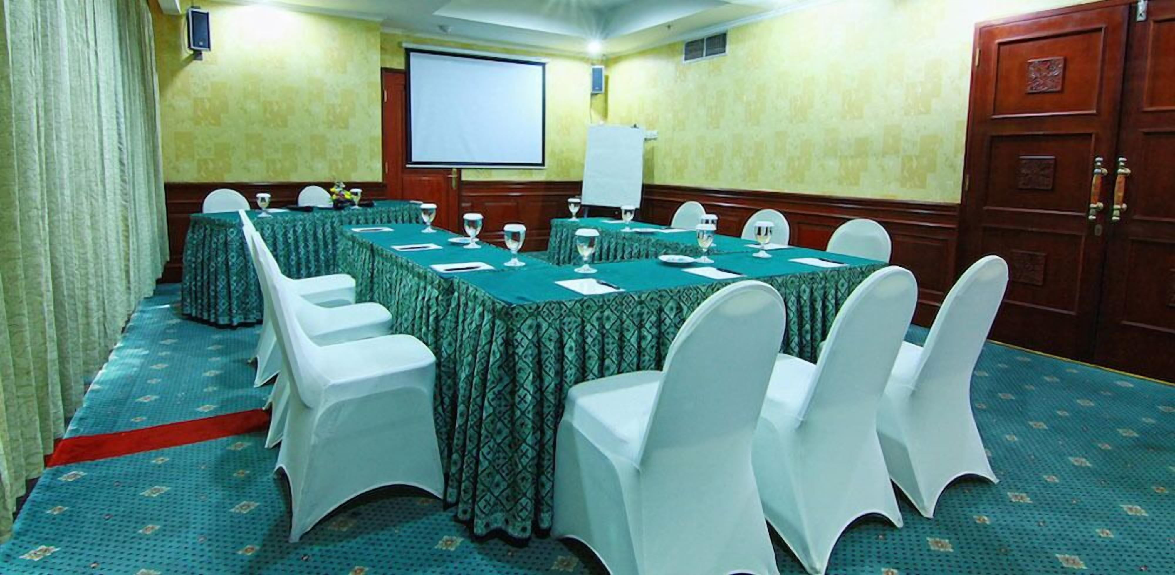 A conference room with a long table, white chairs, a projector screen, and a whiteboard.