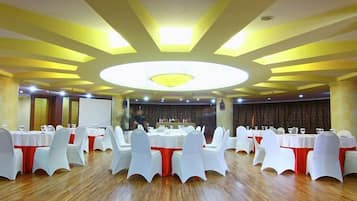 Un salón de banquetes con mesas redondas, sillas blancas y una lámpara circular en el centro del techo.