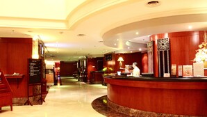Un'area di reception di un hotel con una scrivania a forma di arco, una zona salotto con sedie e un pavimento in marmo lucido.