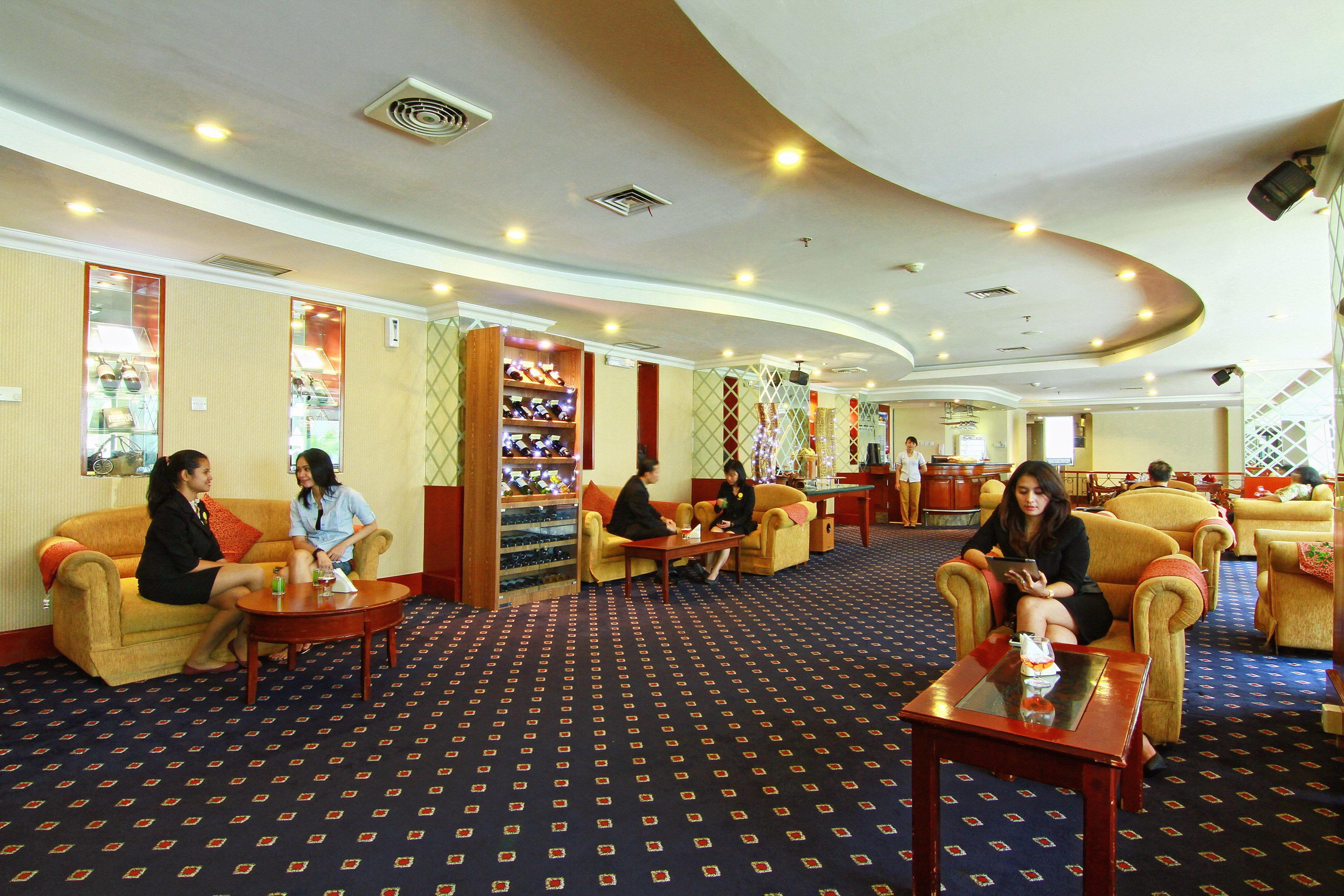 A hotel lobby with multiple seating areas, a reception desk, and a patterned carpet.